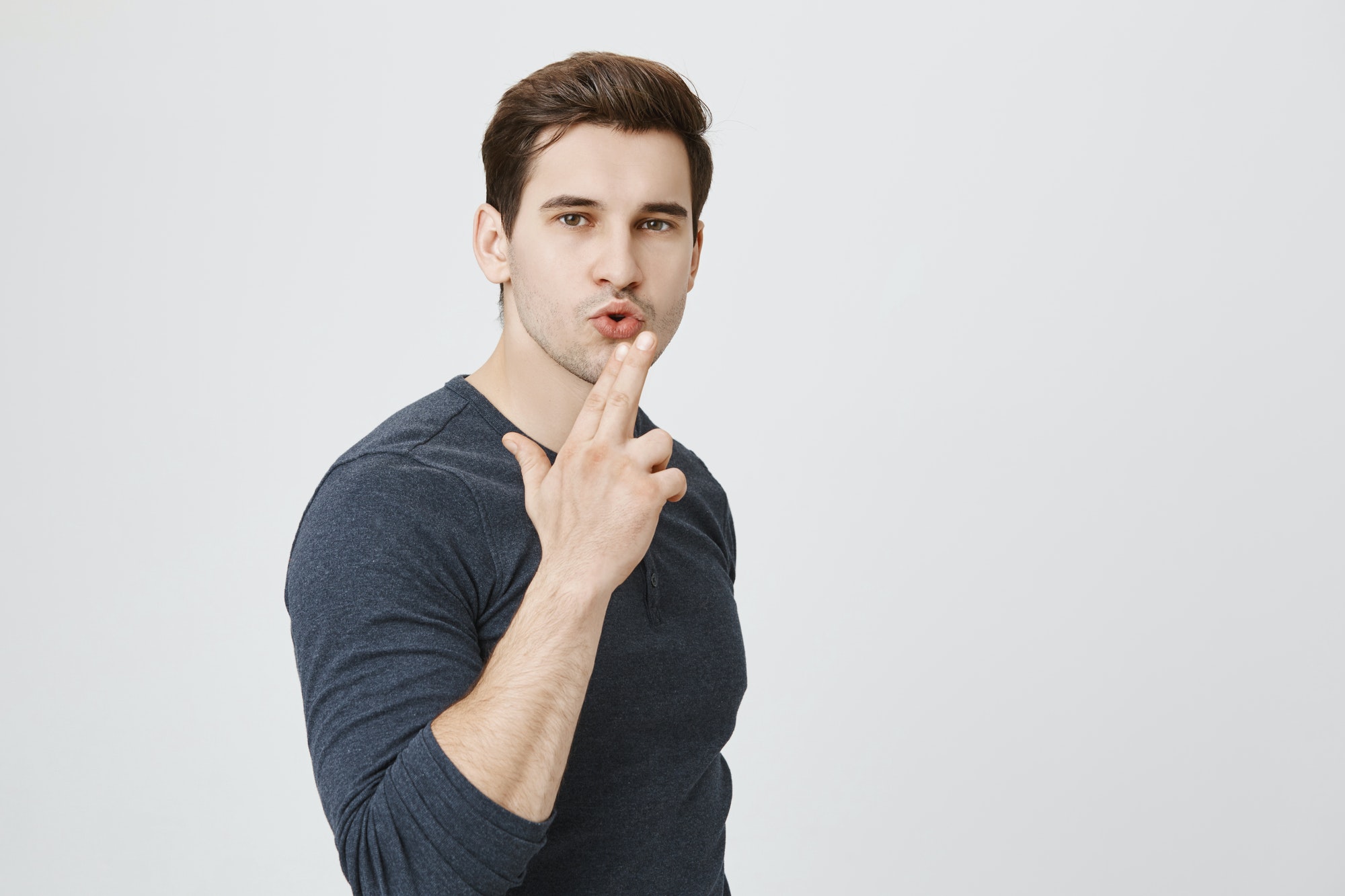 Horizontal portrait of confident young man makes shooting gesture, ready to reach great success
